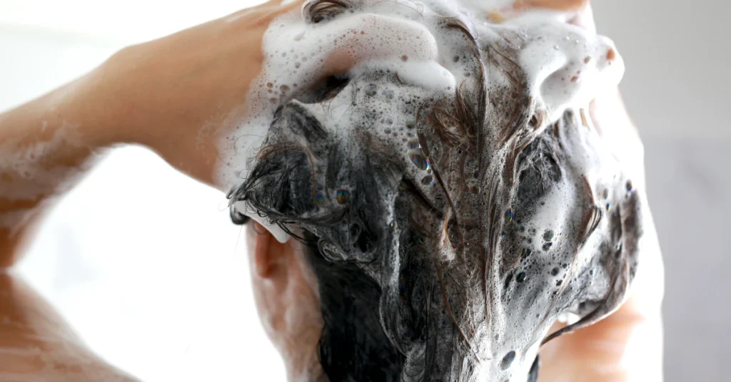 Person washing hair with lukewarm water to prevent scalp dryness