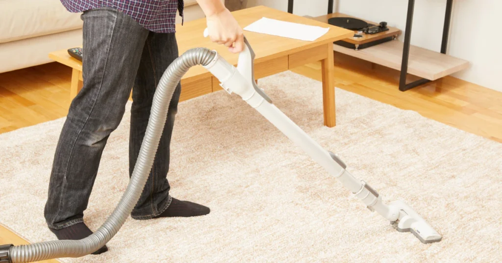 Person vacuuming a carpet with an upright vacuum cleaner
