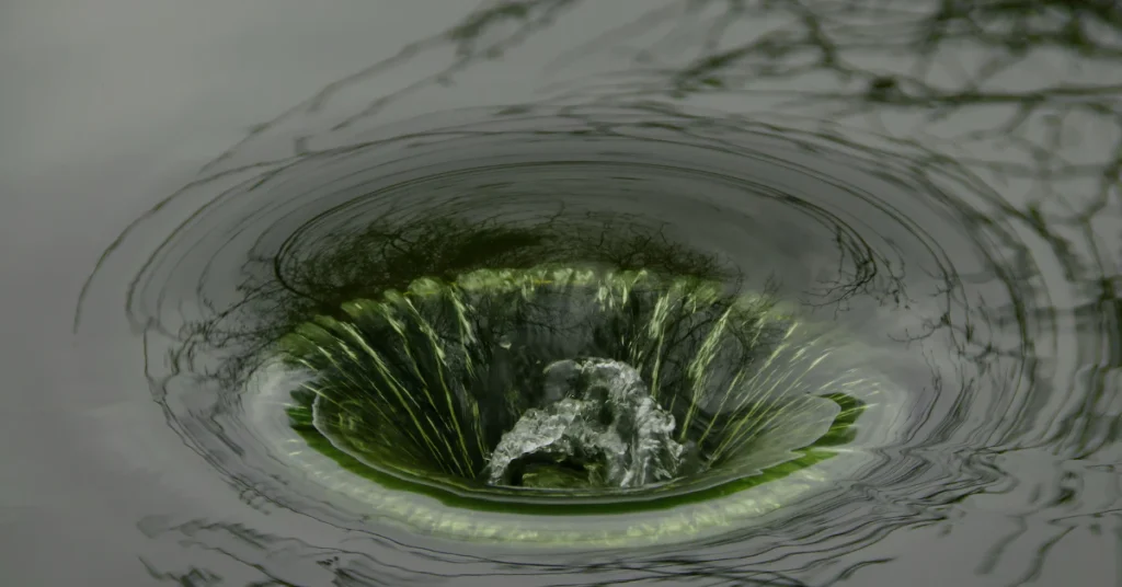 Baking soda and vinegar fizzing down a kitchen sink drain with a kettle of boiling water nearby
