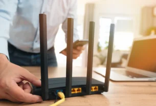 Person adjusting a black WiFi router with antennas on a desk next to a laptop
