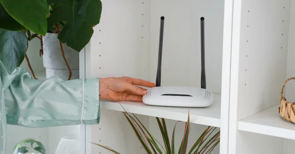 Hand placing a white WiFi router on an open shelf in a central spot