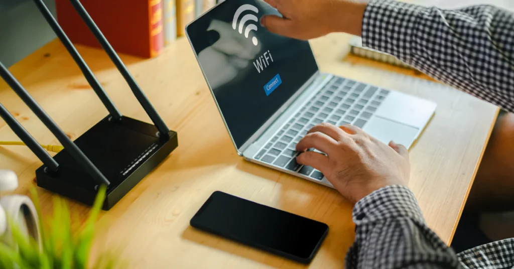 Person using a laptop next to a WiFi router with antennas