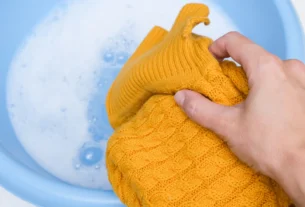 Hand washing a yellow wool sweater in a basin of cold soapy water
