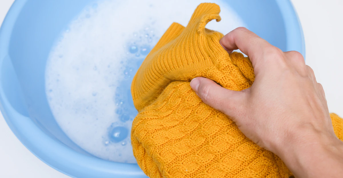 Hand washing a yellow wool sweater in a basin of cold soapy water