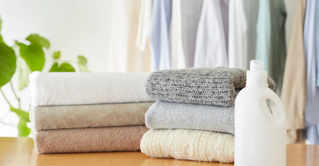 Neatly folded wool sweaters beside a bottle of gentle wool detergent