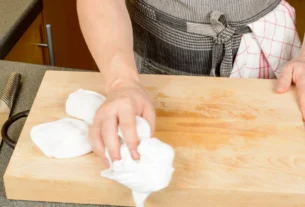 Person wiping a wooden cutting board with a cloth while cleaning the kitchen counter
