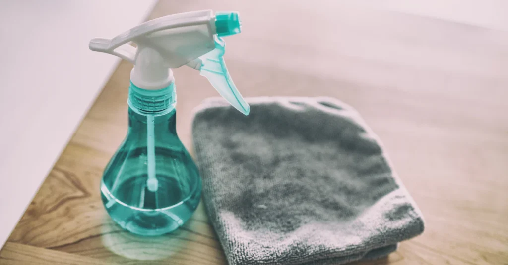 Teal spray bottle of sanitizing solution next to a folded gray cleaning cloth