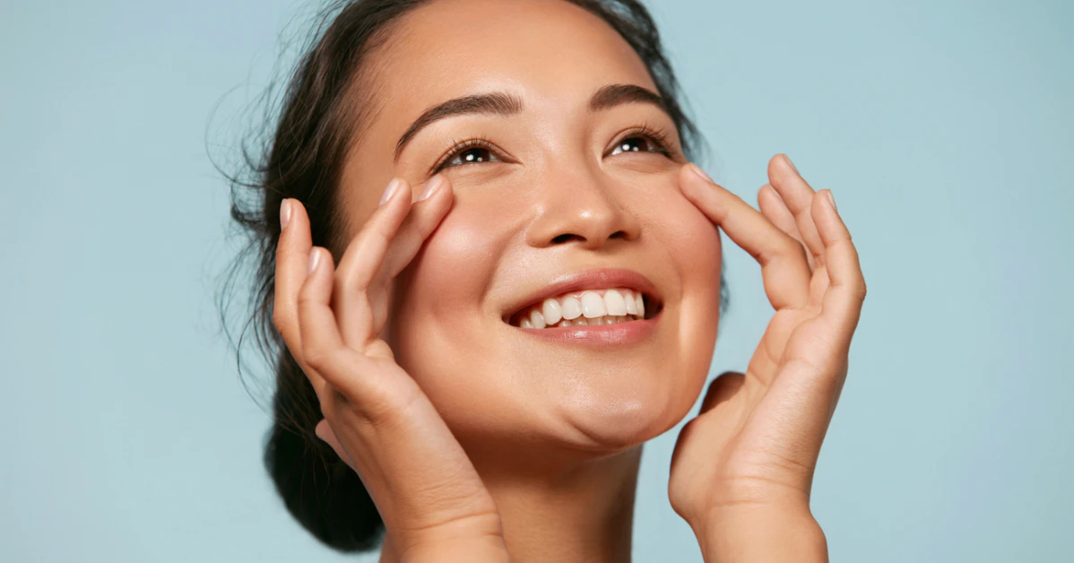 Smiling woman touching her clear, healthy-looking skin against a light blue background
