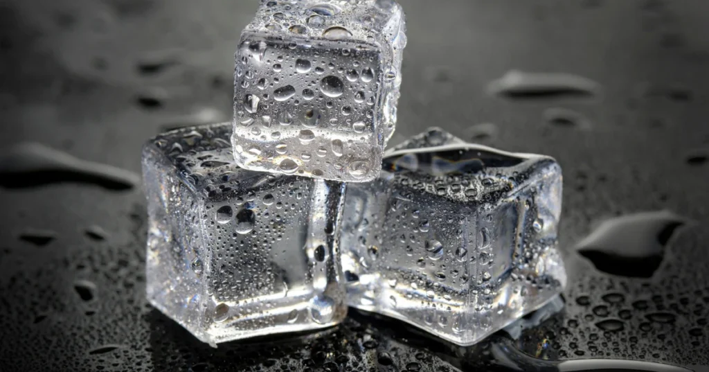 Ice cubes on a dark wet surface, used to reduce swelling and redness in inflamed pimples