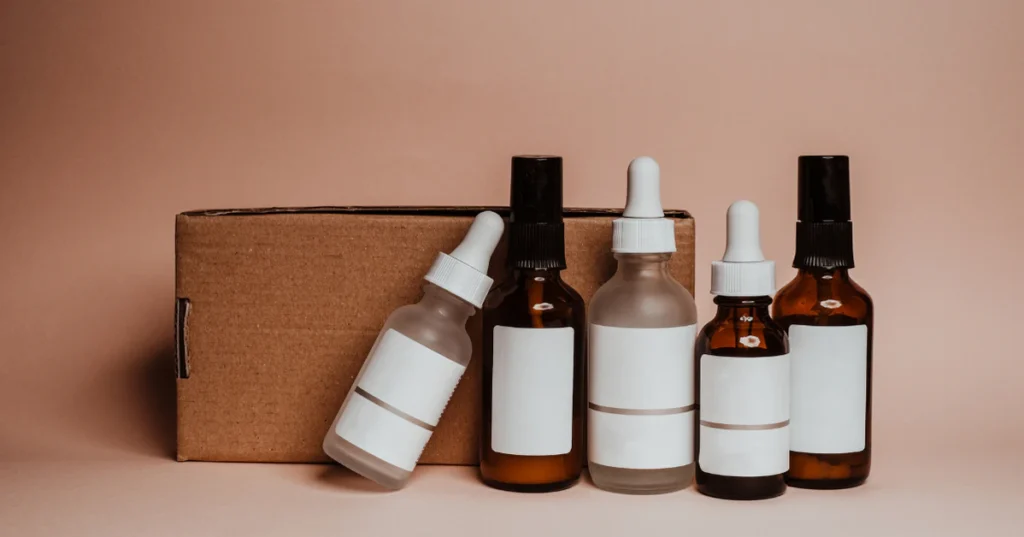 Skincare serum and dropper bottles lined up beside a cardboard box on a beige background