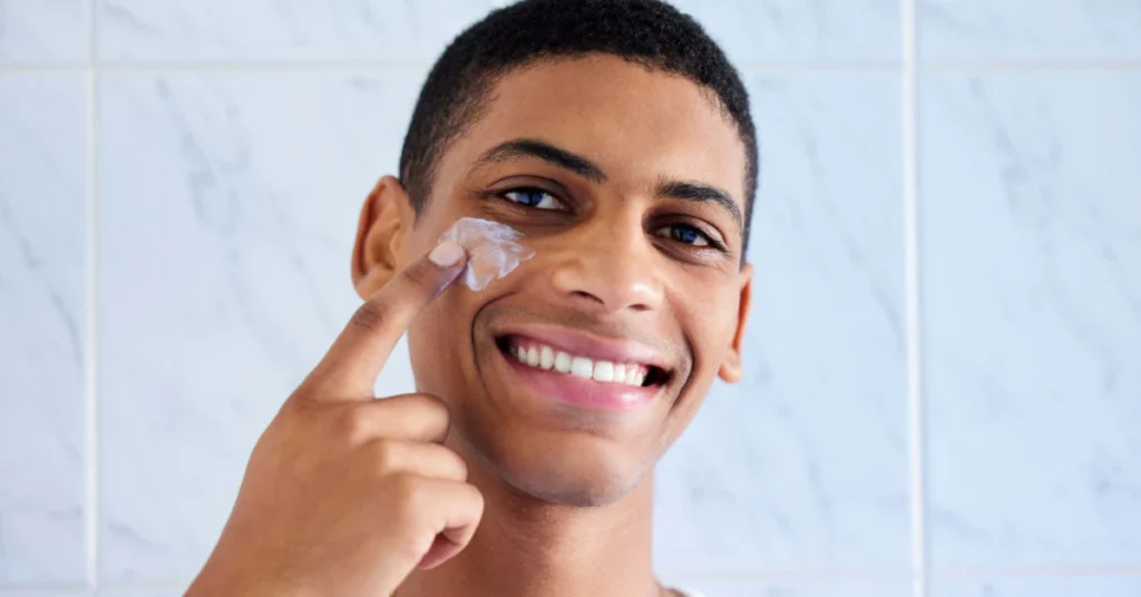 Smiling man applying skincare cream under his eye