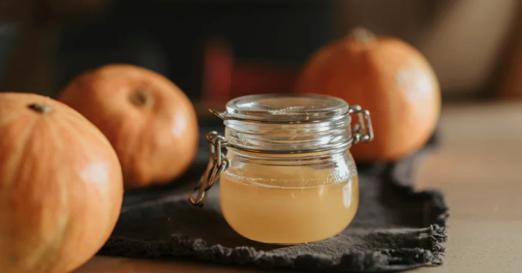 Small jar of apple cider vinegar beside oranges, used as a fruit fly vinegar trap