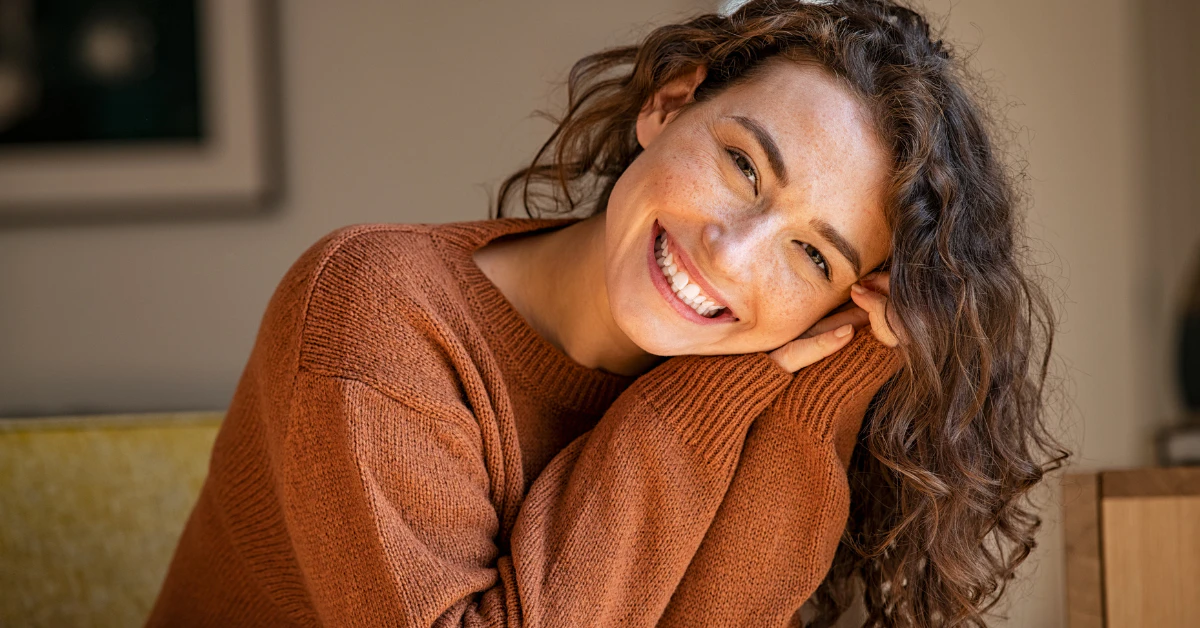 Smiling woman with curly hair resting her head on her hand