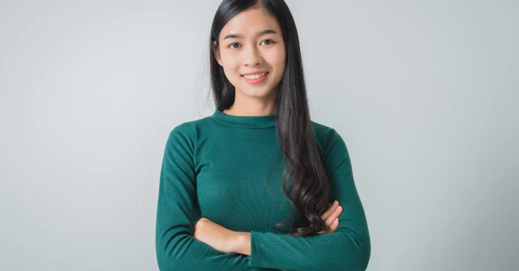 Young woman with long dark hair standing with arms crossed in a green sweater