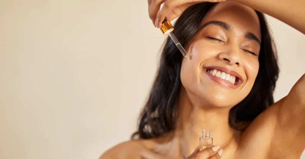 Woman with glowing skin smiling with eyes closed and hand raised near her head