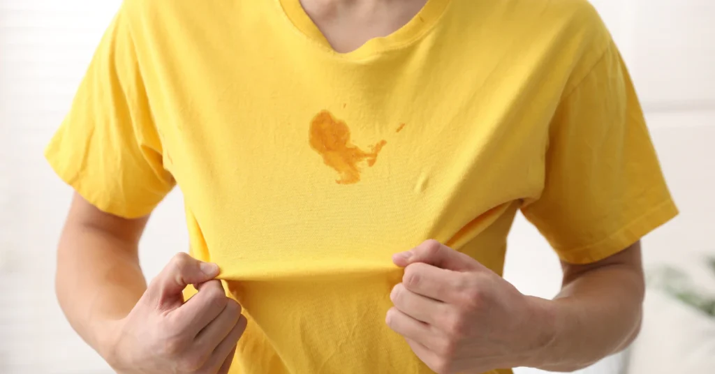 Person holding up a yellow t-shirt with a stain on the front after washing