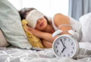 Person sleeping peacefully with an eye mask next to an alarm clock