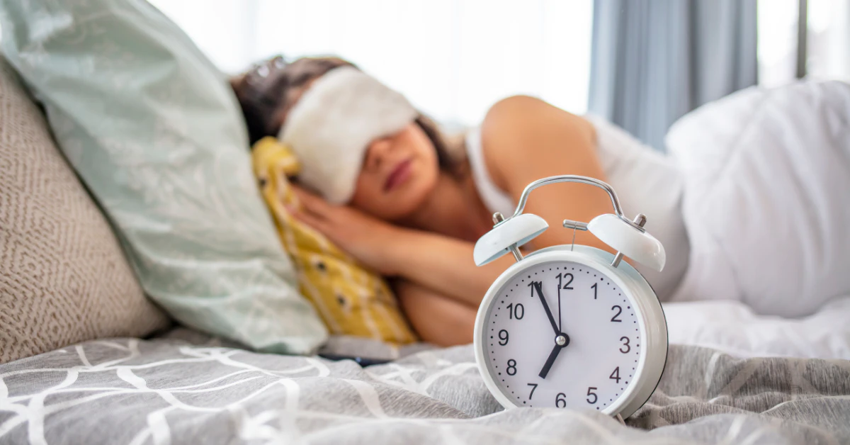 Person sleeping peacefully with an eye mask next to an alarm clock