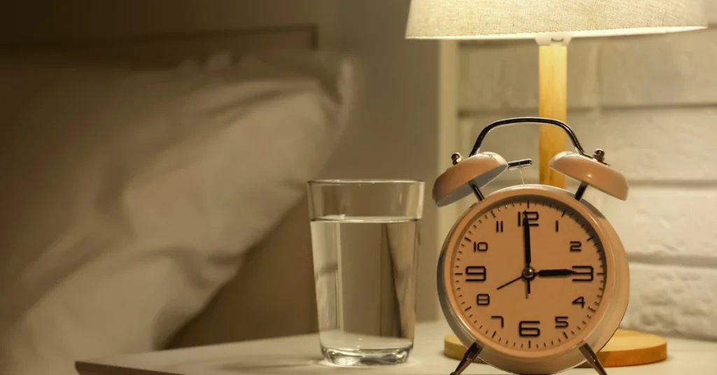 Alarm clock and a glass of water on a bedside table at night