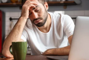 Tired man rubbing his forehead at a desk with a laptop