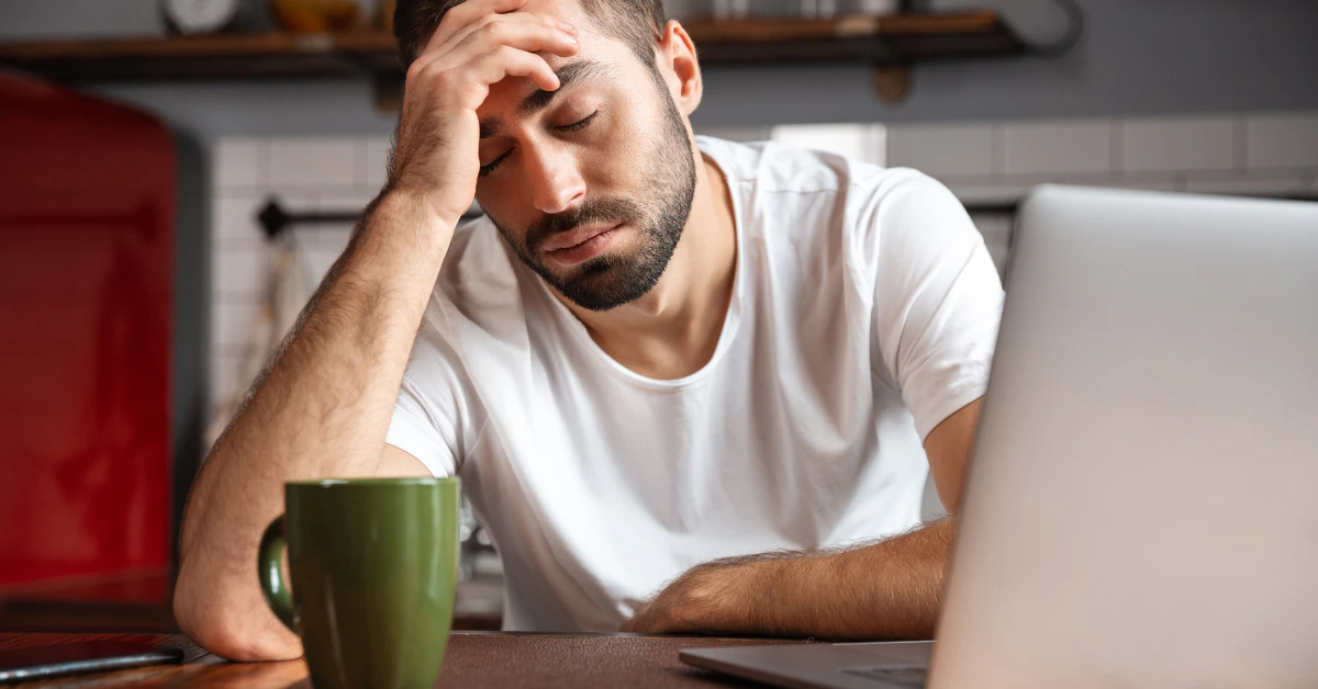 Tired man rubbing his forehead at a desk with a laptop