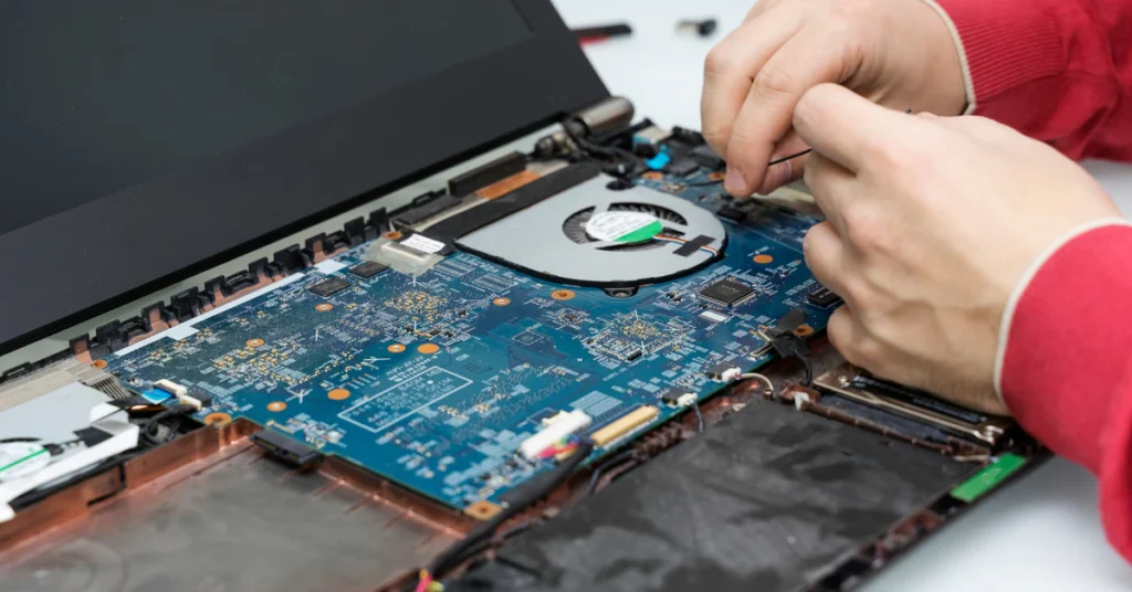 Hands working on the motherboard of an open laptop during a repair