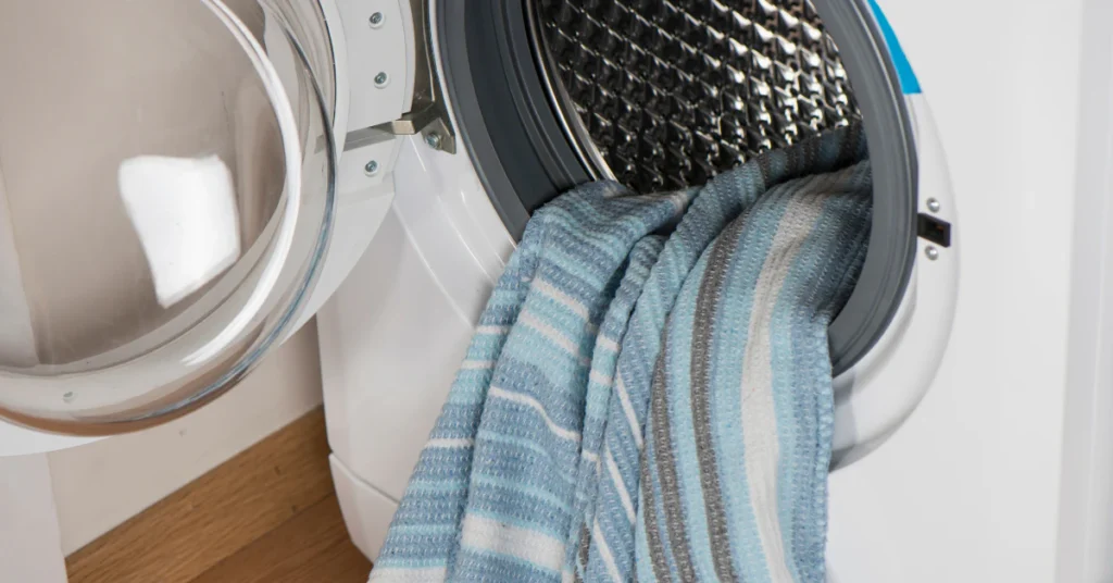 Front-load washing machine with a blue striped blanket hanging out of the open door