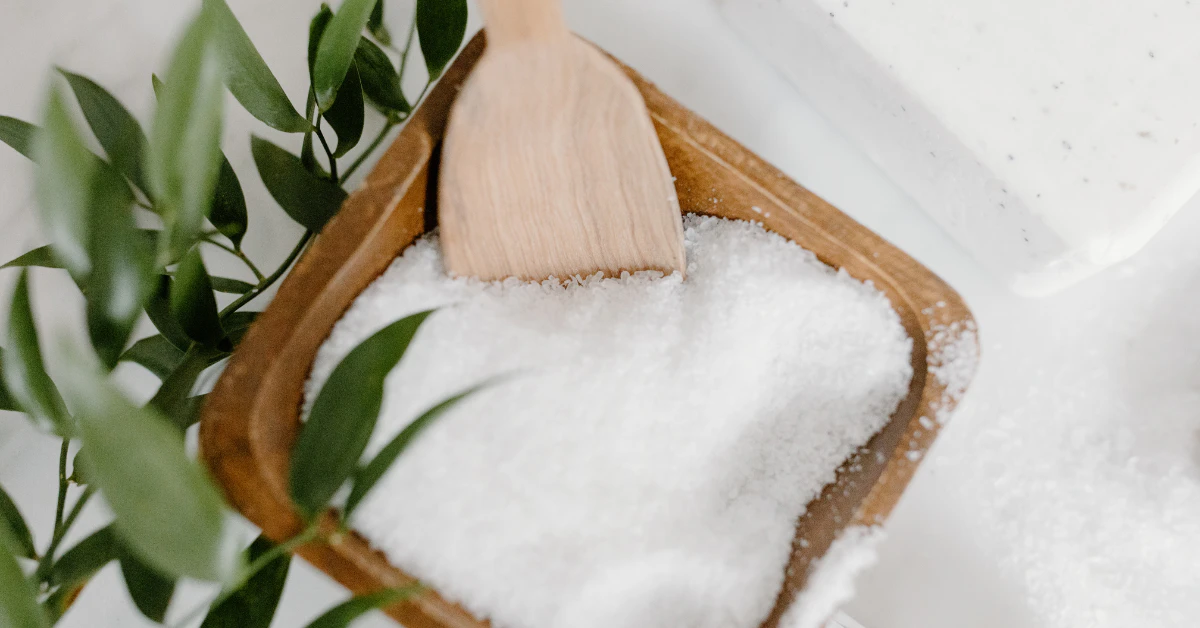 White crystalline salt powder in a wooden scoop, representing smelling salts made from ammonium carbonate