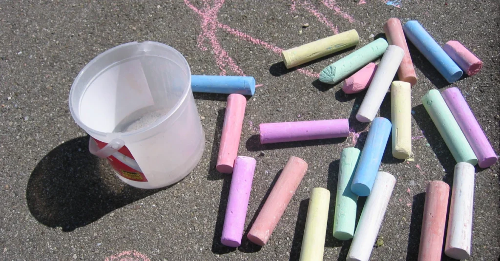 Colorful chalk sticks and a plastic cup on a dark surface